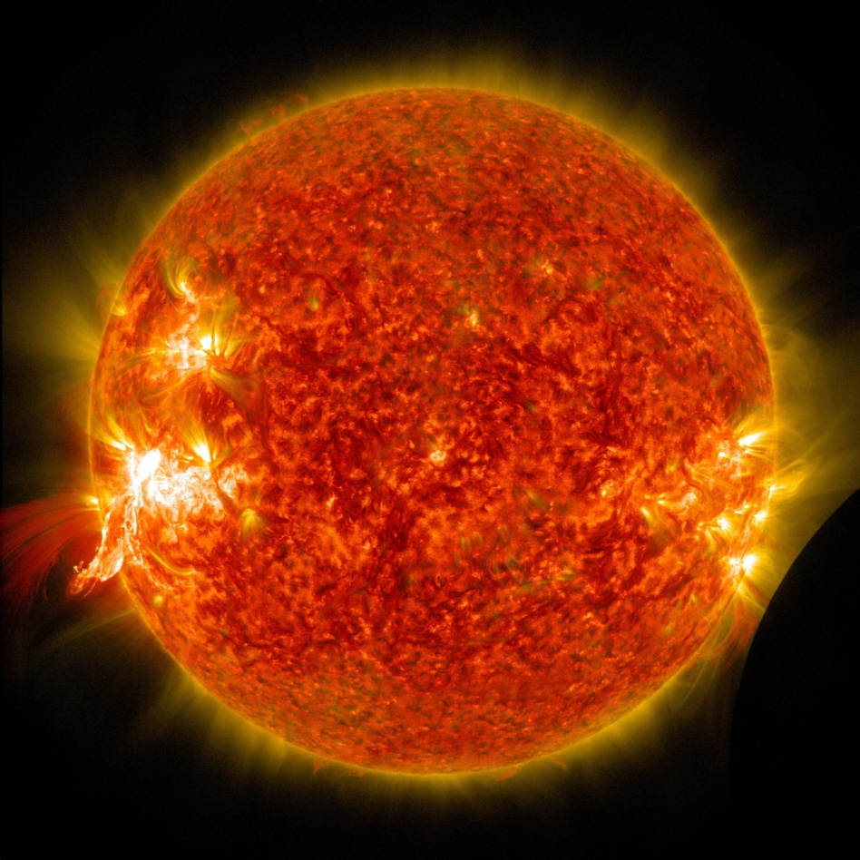 A solar flare erupts on Jan. 30, 2014, as seen by the bright flash on the left side of the sun, captured here by NASA's Solar Dynamics Observatory. In the lower right corner the moon can be seen, having just passed between the observatory and the sun.