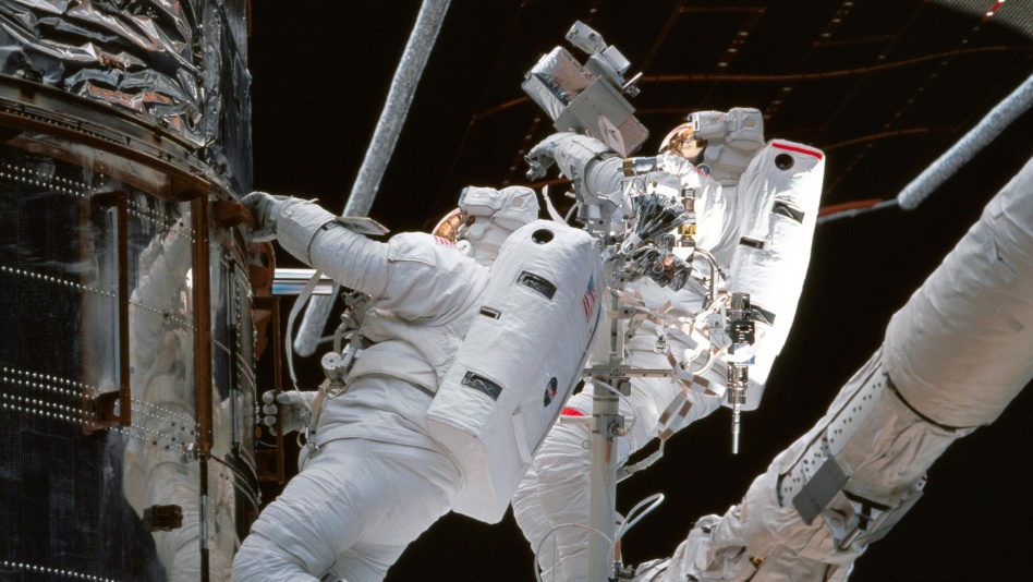 TS082-738-054 (11-21 Feb. 1997) --- As photographed from inside the Space Shuttle Discovery?s crew cabin, astronauts Steven L. Smith (left) and Mark C. Lee (red stripe) inspect insulation around Bay 10 of the Hubble Space Telescope (HST) during one of five days of extravehicular activities (EVA) designed to service the HST.